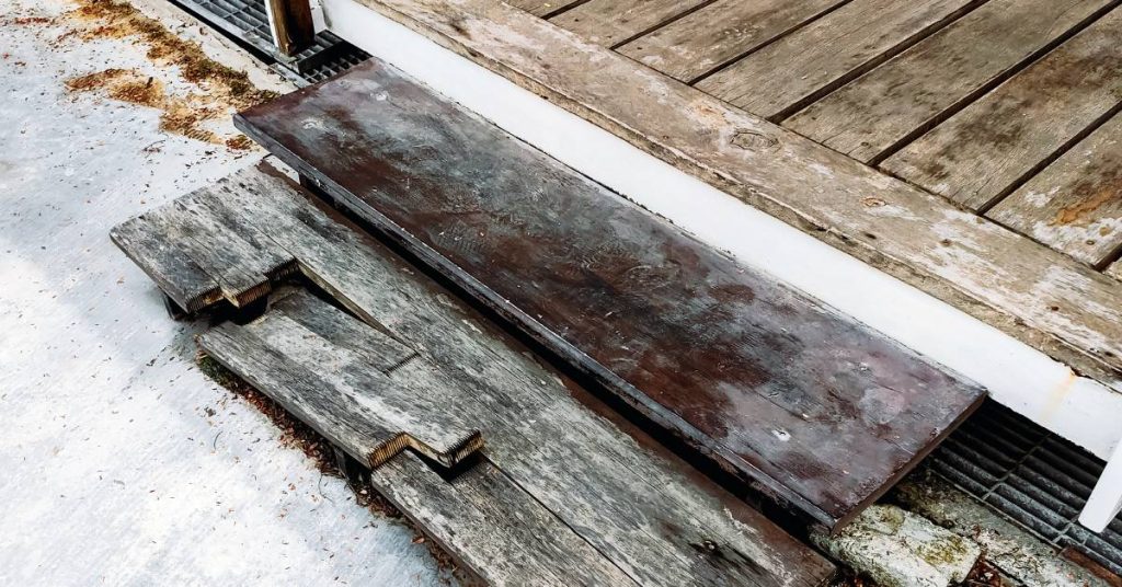 A set of steps leading up to a porch on a log cabin. The first one is broken after weakening due to fungus.